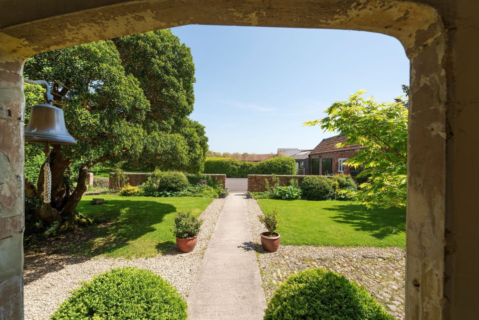 View through a stone archway of a garden path leading to a manor house.