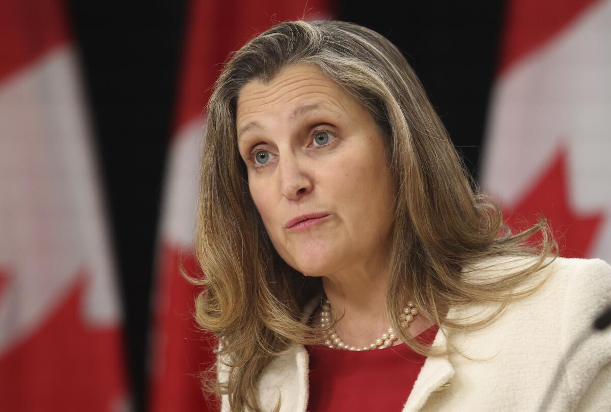 A woman speaks, with Canadian flags in the background.