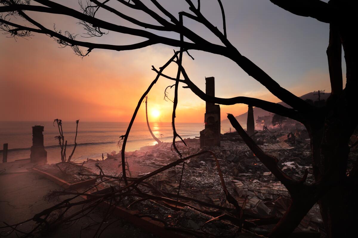 The ruins of beachfront homes smolder as the sun sets in the Pacific Ocean.