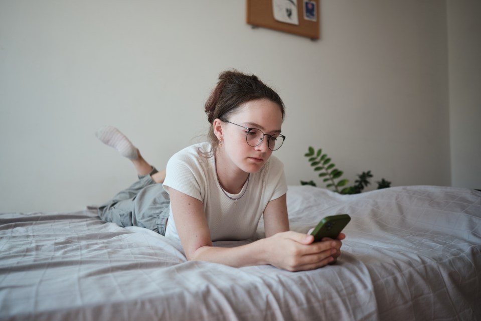 Sad teenager lying on bed using a cellphone.