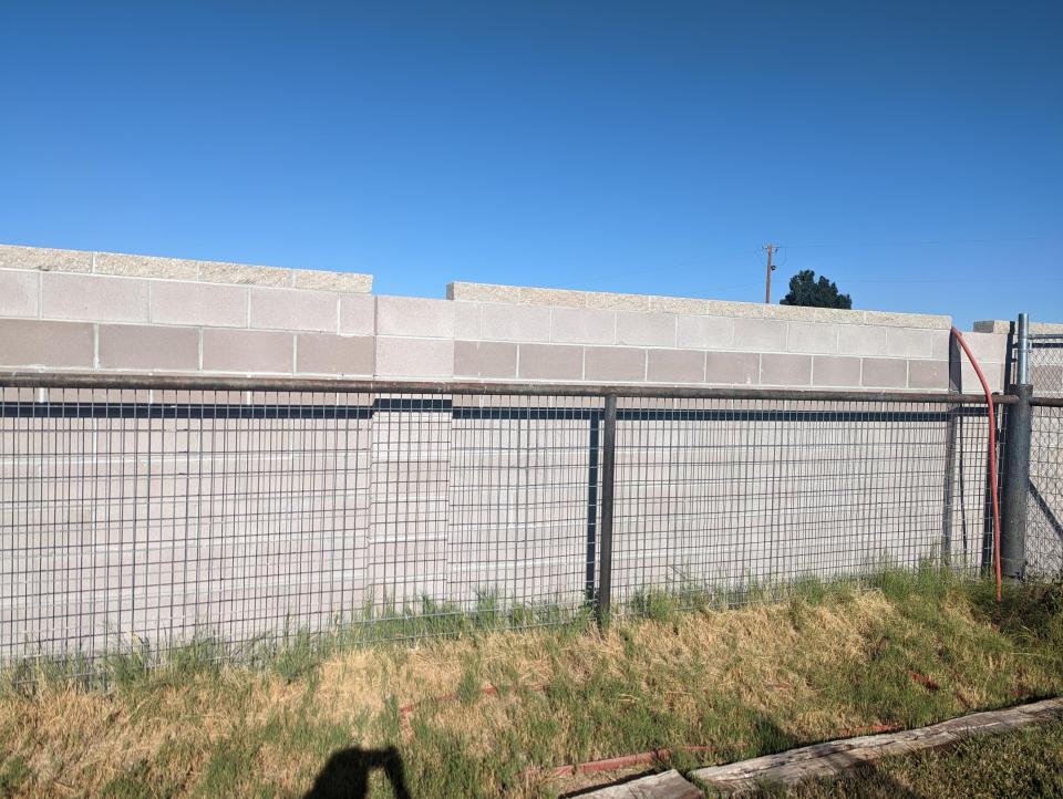 A newly constructed block wall next to a wire fence.