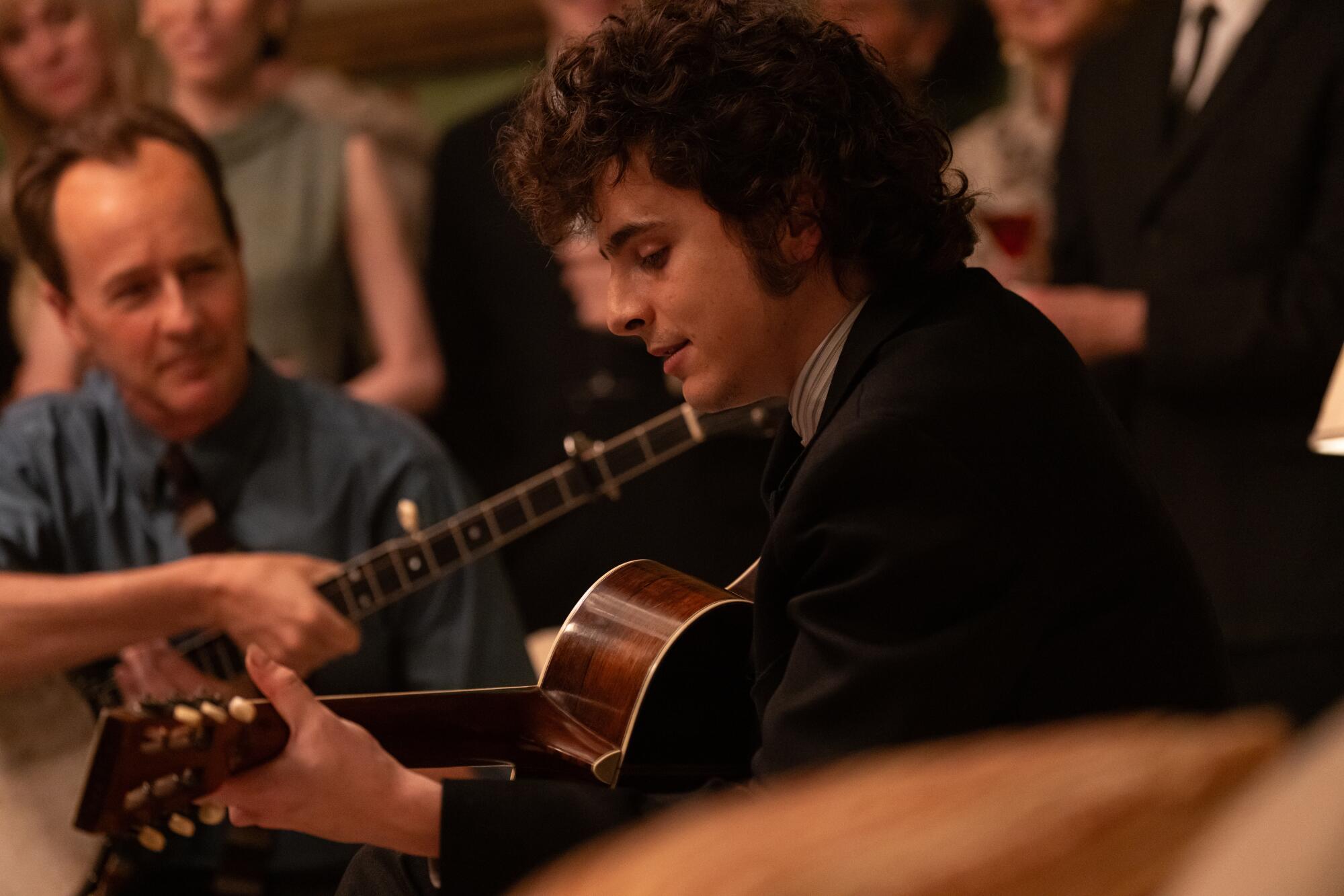 Timothee Chalamet plays guitar as Bob Dylan in "A Complete Unknown."