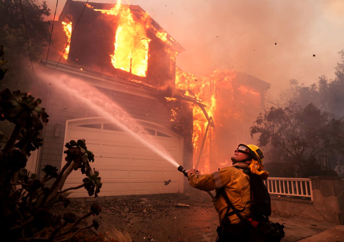 Firefighters battle a house fire off Bollinger Drive in Pacific Palisades, CA after a brush fire, called the Palisades fire