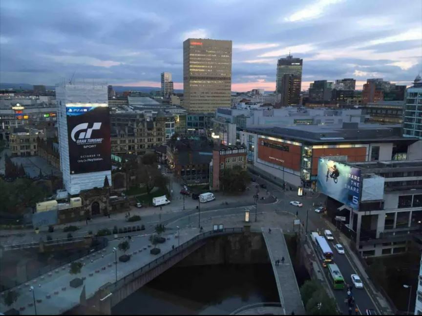 Aerial view of a city at dusk, featuring a large Gran Turismo Sport advertisement on a building.