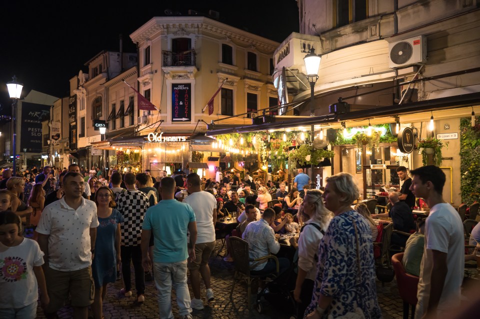 People enjoying a warm evening at outdoor cafes in Bucharest's old town.