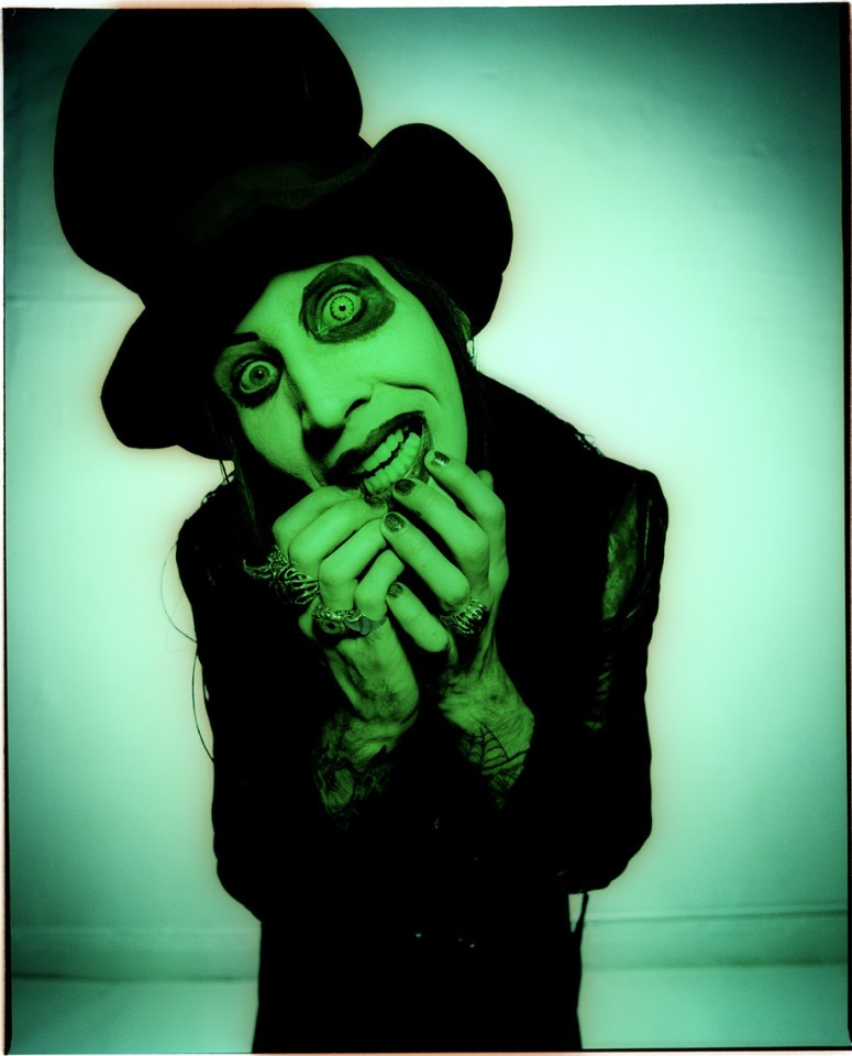 Portrait of Manson in a green top hat, hands to face.