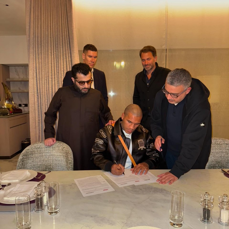 Conor Benn signing a document, watched by several men.