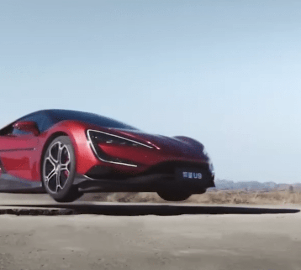 Red Yangwang U9 sports supercar driving over a pothole.