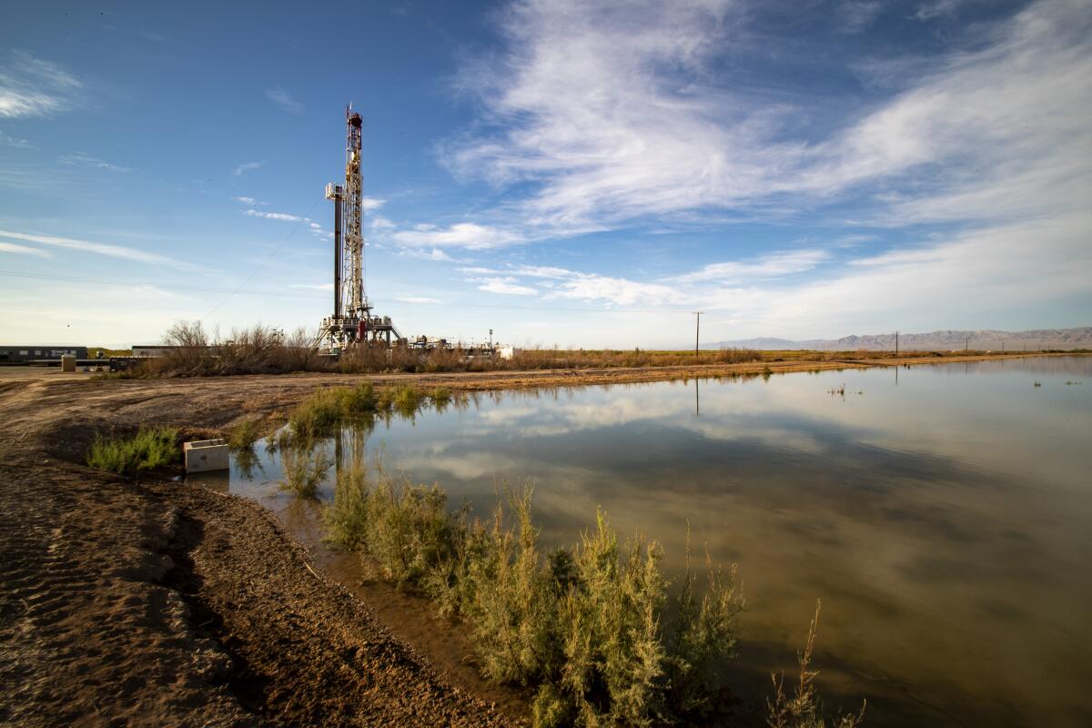 A drilling rig rises behind a lake