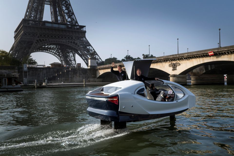 Two men in an electric Sea Bubble flying taxi on the Seine River in Paris, with the Eiffel Tower in the background.