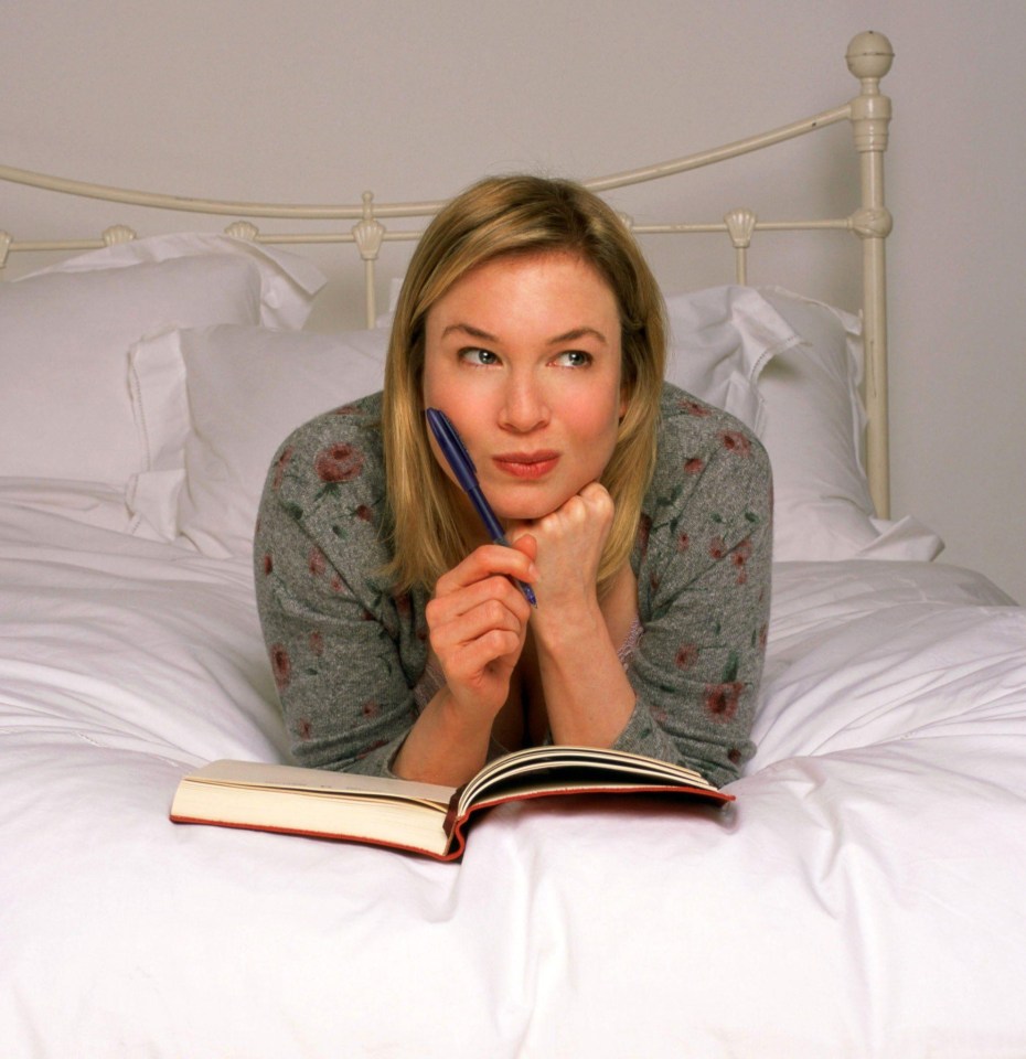 Renee Zellweger lying in bed, pensively holding a pen and open diary.