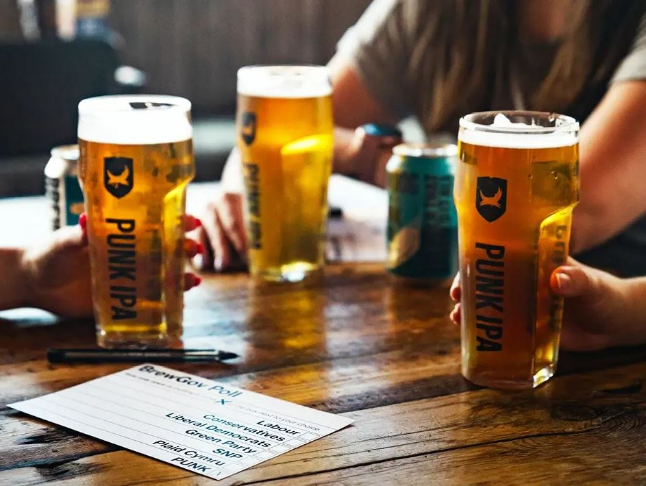 People holding pints of Punk IPA beer at a table with a ballot.