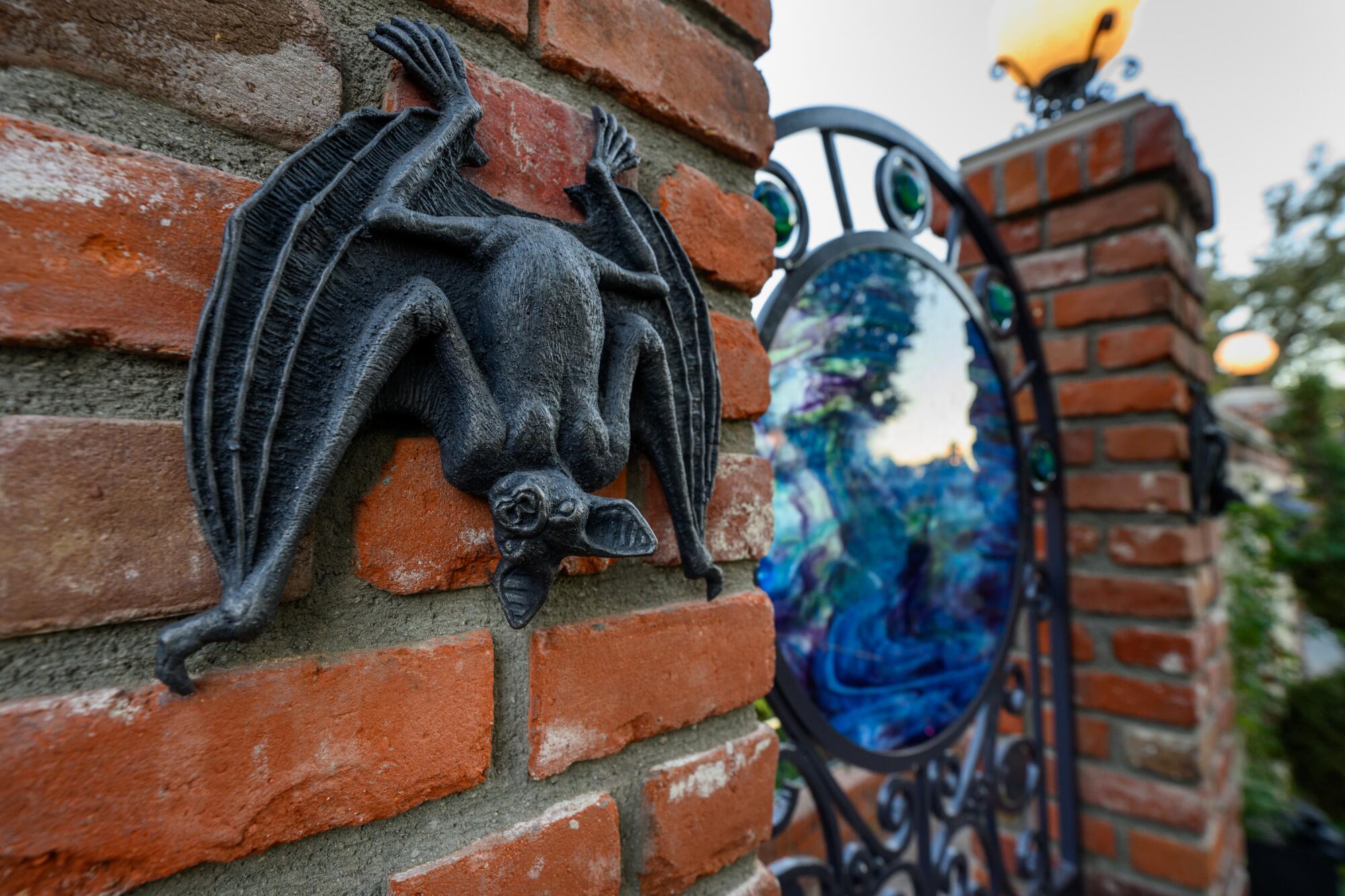 A bat statue on a brick wall next to a mystical gate. 