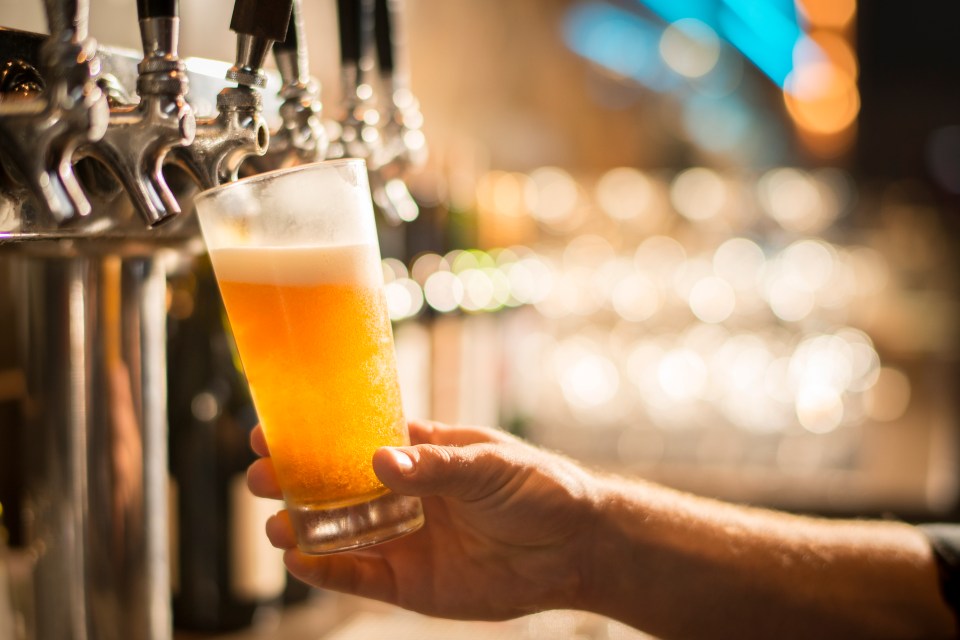 A hand holding a pint glass of beer being poured from a tap.