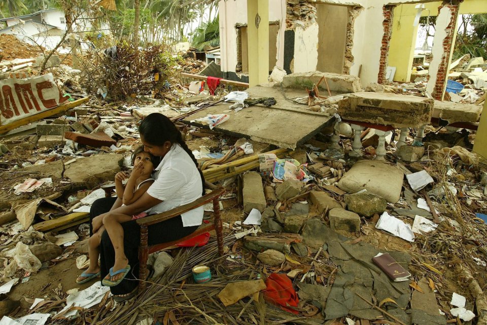 A mother and child sit amidst the rubble of their tsunami-damaged home.