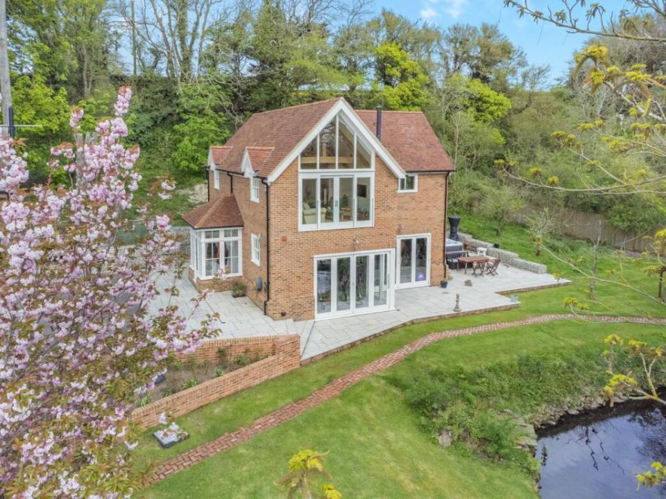 Aerial view of a brick house with a patio and pool, next to a river.