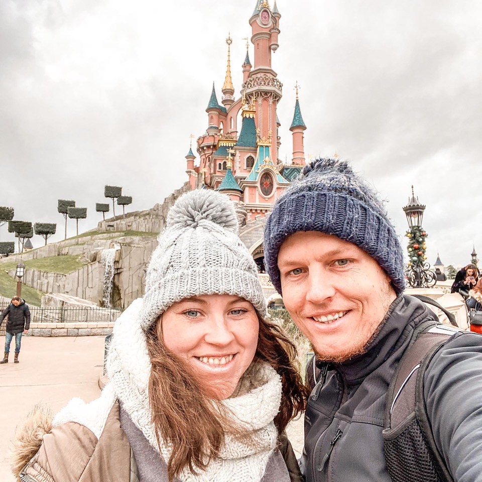 Couple in winter hats in front of Sleeping Beauty Castle at Disneyland Paris.