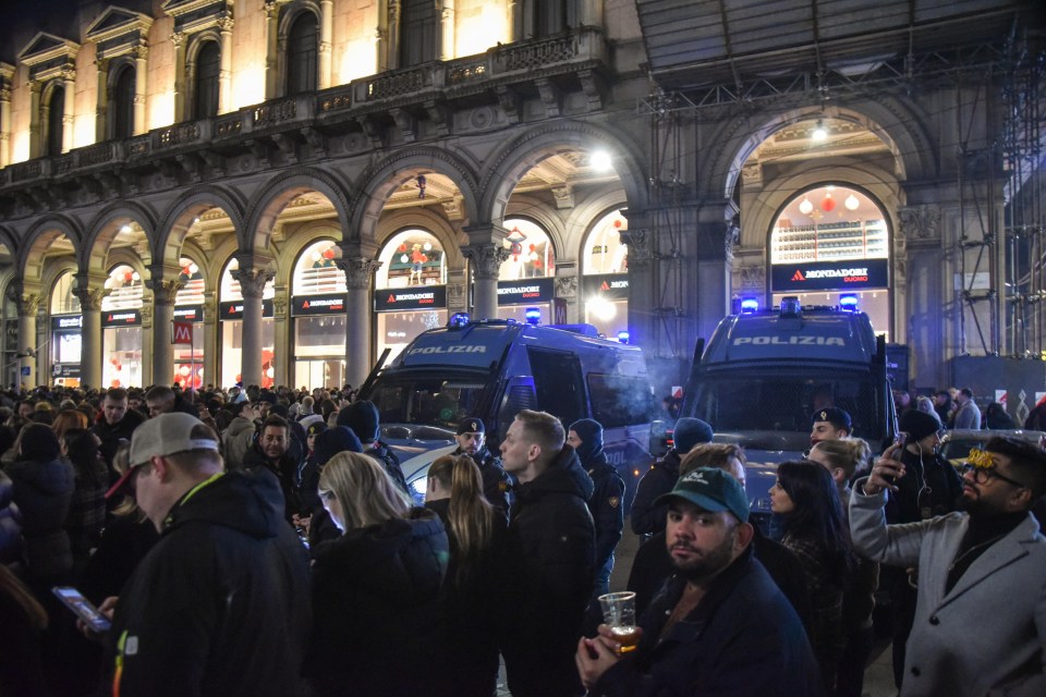 Police vehicles near a crowd of people in Milan, Italy.