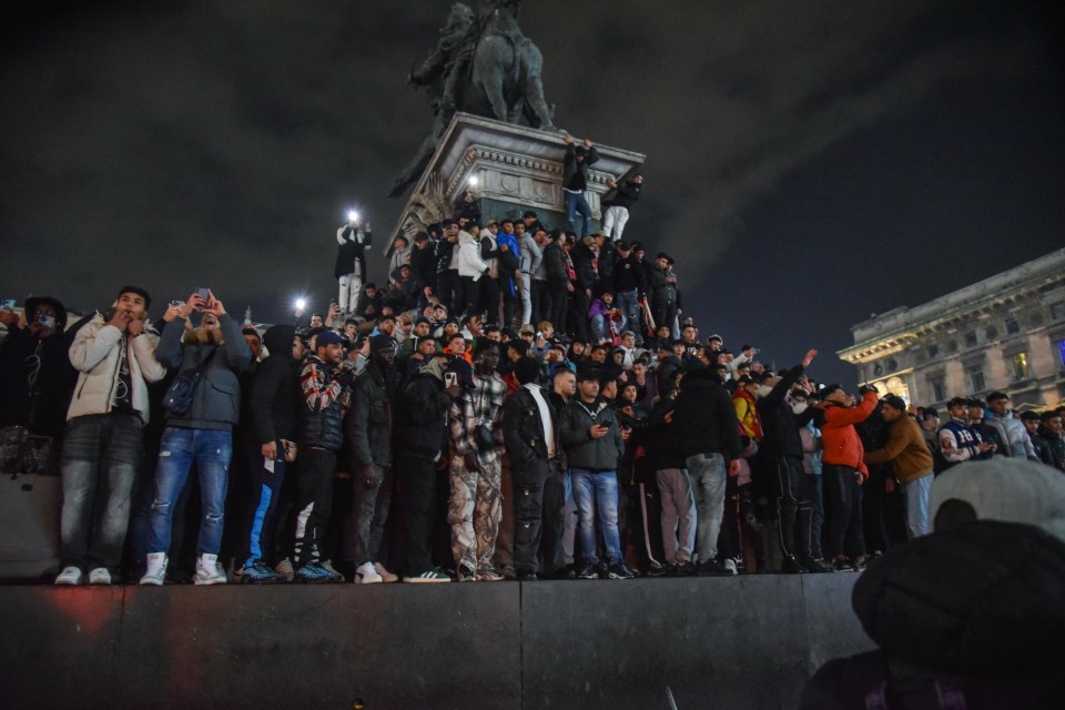 Large crowd of people gathered in Duomo Square, Milan, at night.