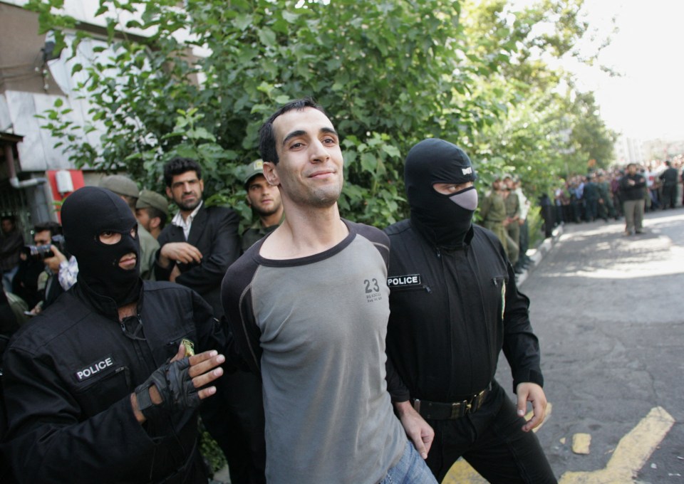 A man in custody escorted by masked Iranian policemen.