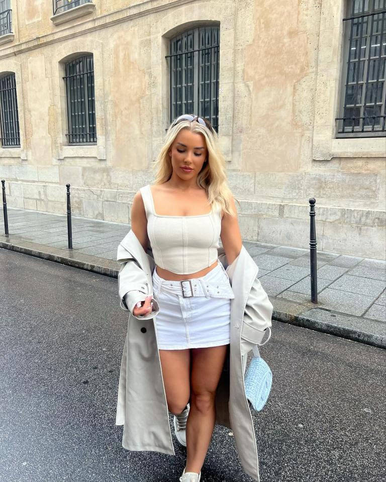 a woman in a white top and white skirt is walking down a street