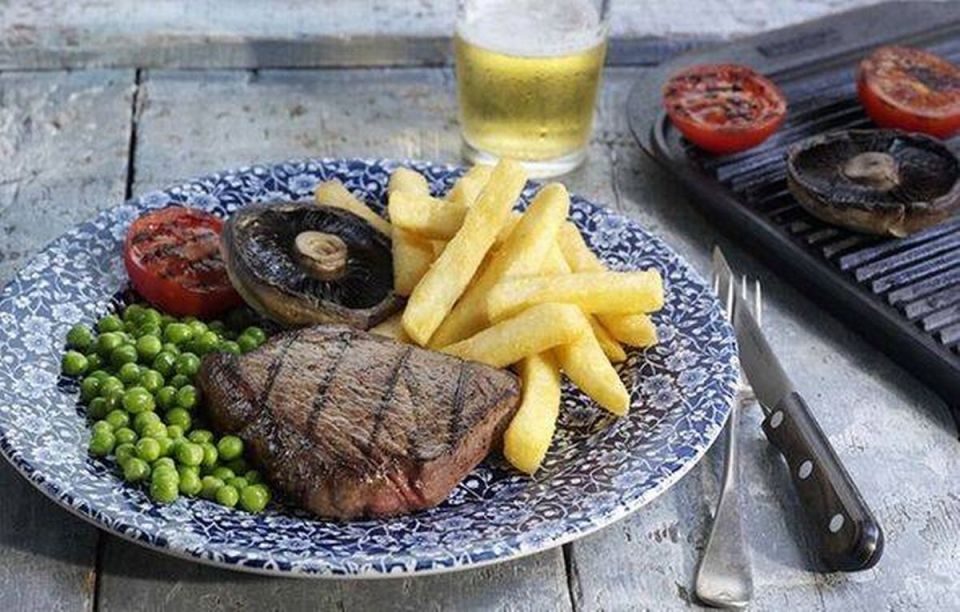 Steak, fries, peas, mushrooms, and tomatoes on a plate.