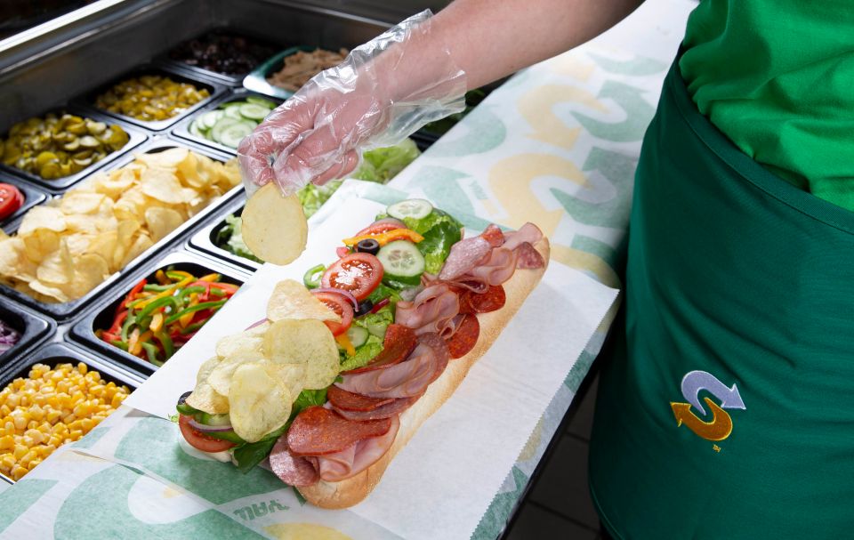 A Subway employee adding potato chips to a sub.