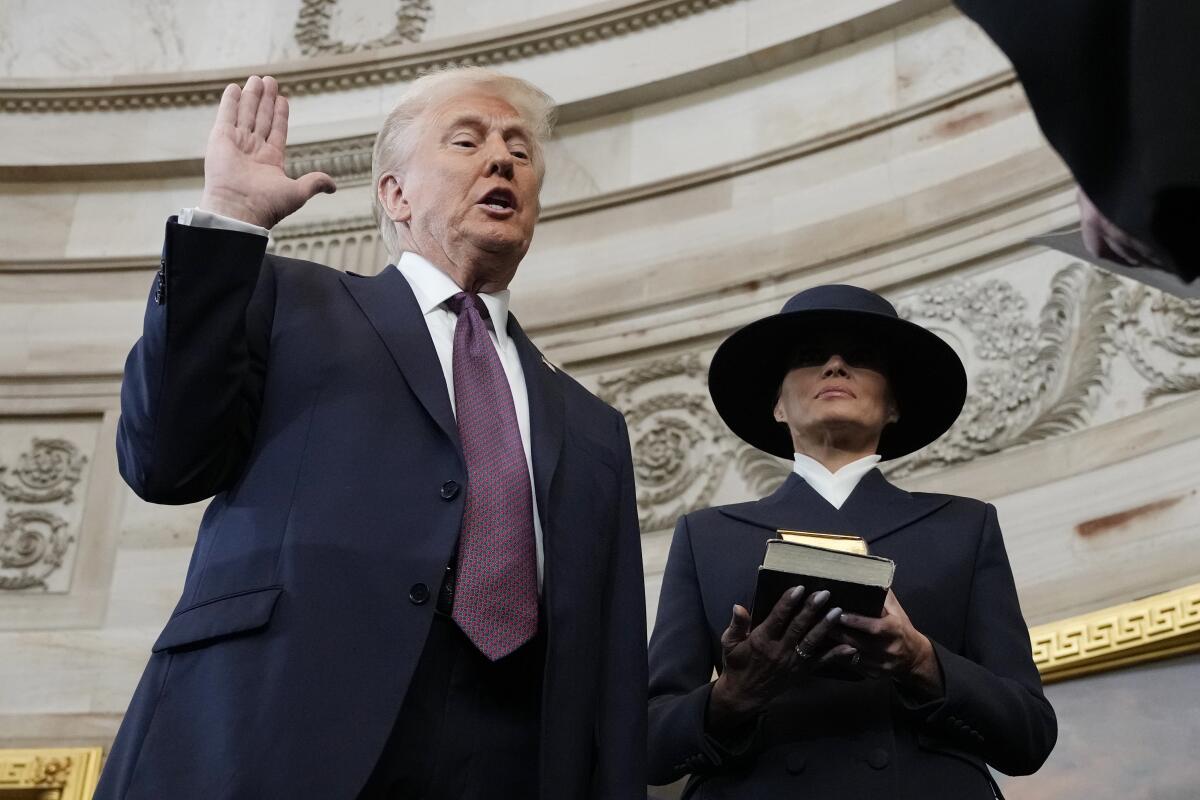 President Trump takes the oath of office while Melania Trump holds a Bible 