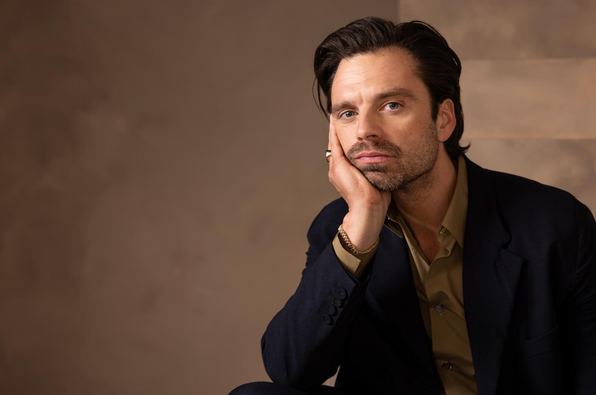 Sebastian Stan rests his chin in his hand for a portrait.