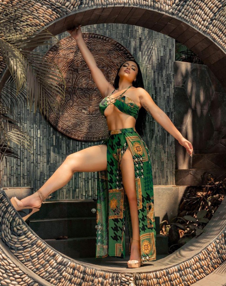 Woman in green patterned outfit posing in a stone archway.