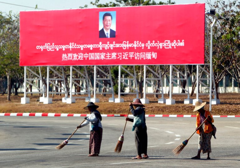 Municipal workers sweep on a road near a welcoming billboard to Chinese President Xi Jinping Friday, Jan. 17, 2020, in Naypyitaw, Myanmar. China's President Xi Jinping was heading to Myanmar on Friday for a state visit likely to deepen the countries' already close bilateral relations at a critical time. (AP Photo/Aung Shine Oo)