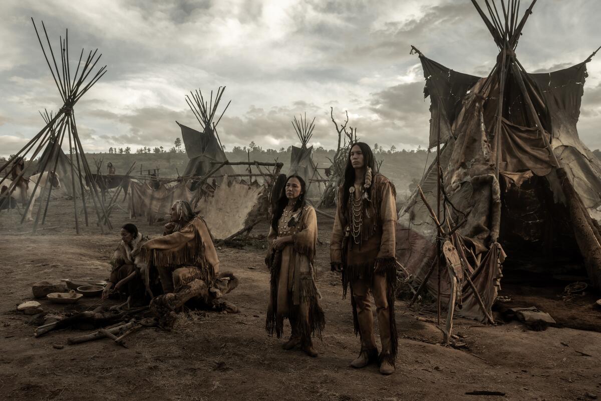 Native Americans standing near teepees.