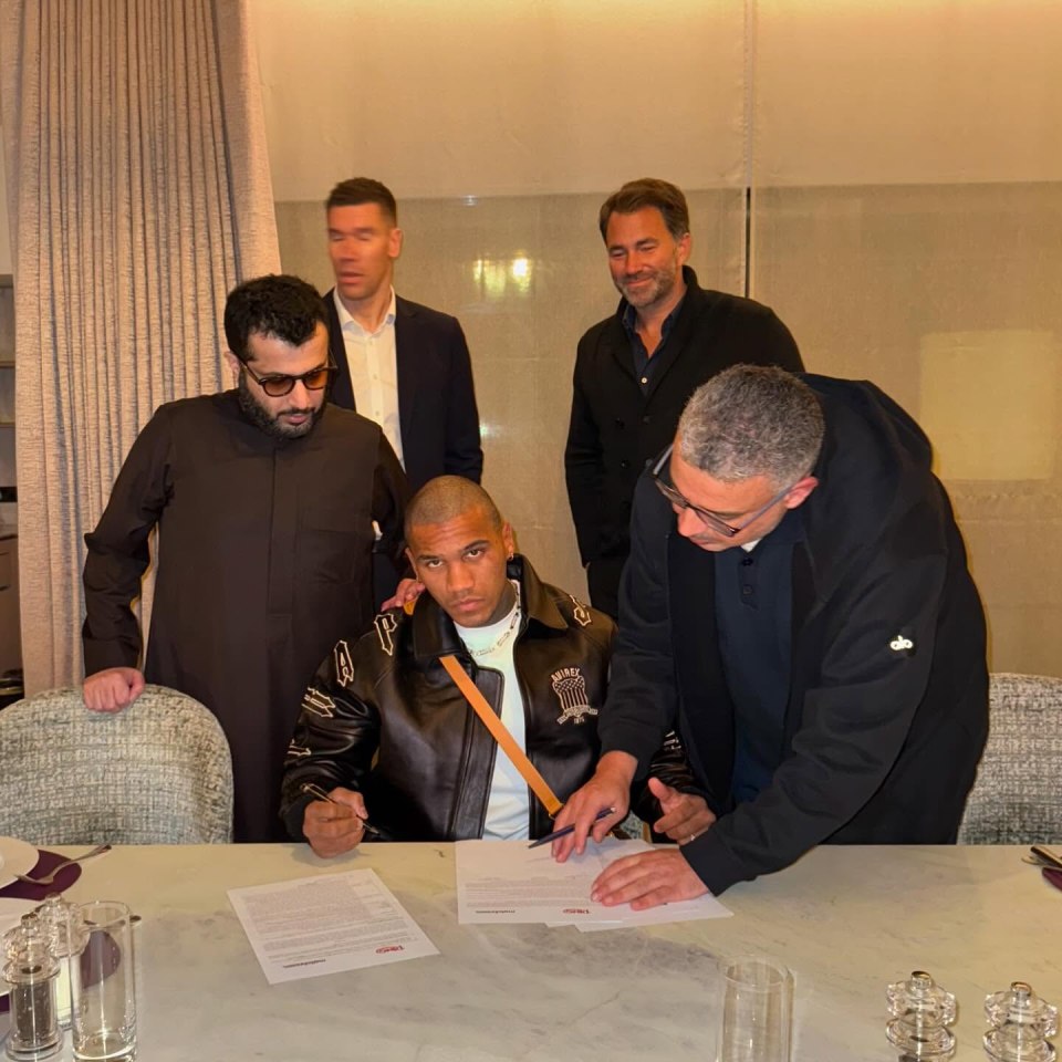 Conor Benn signing a document, watched by several men.