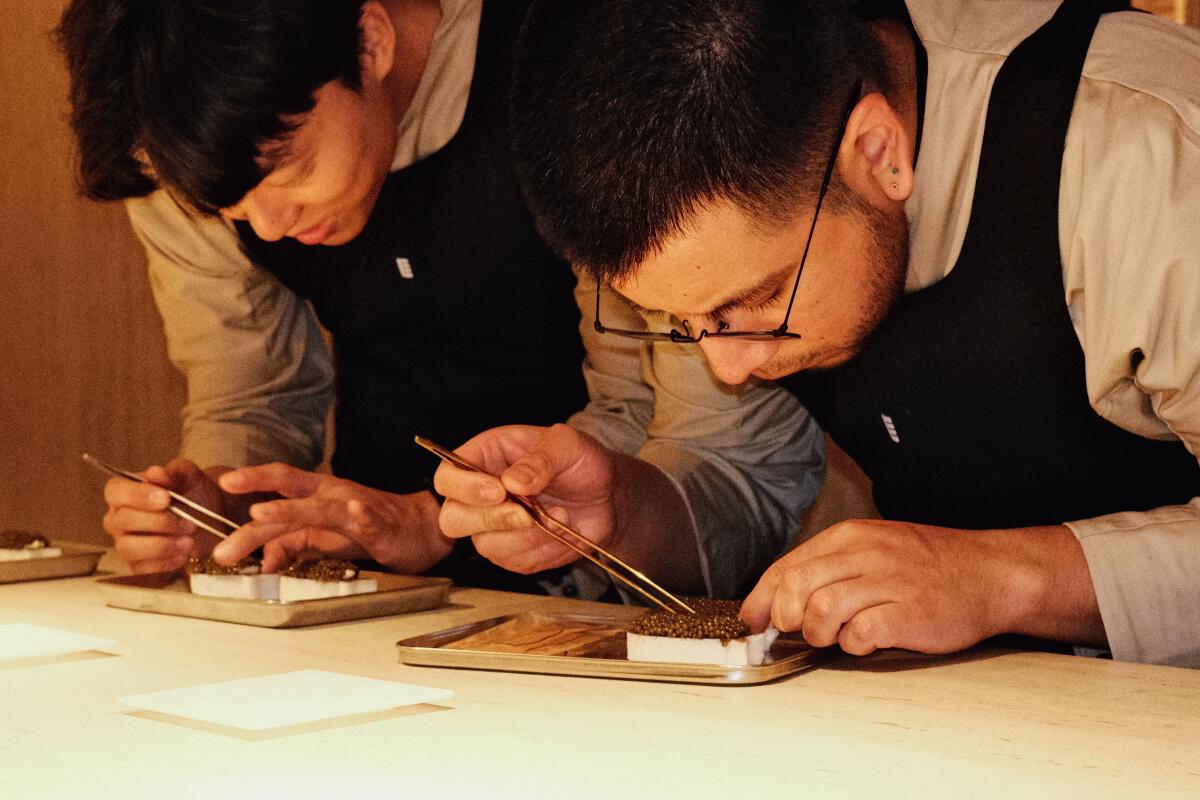 Two men with tweezers prepare the caviar course at Somni in West Hollywood.