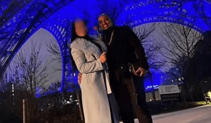 Photo of a man and woman in front of the Eiffel Tower at night.