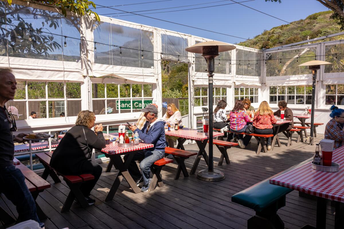 Customers dine on a patio at tables with red-checkered tablecloths.