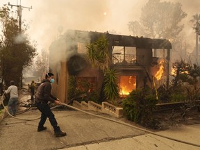 Pedestrians help a firefighter stretch a hose as an apartment building burns, Wednesday, Jan. 8, 2025, in the Altadena section of Pasadena, Calif.