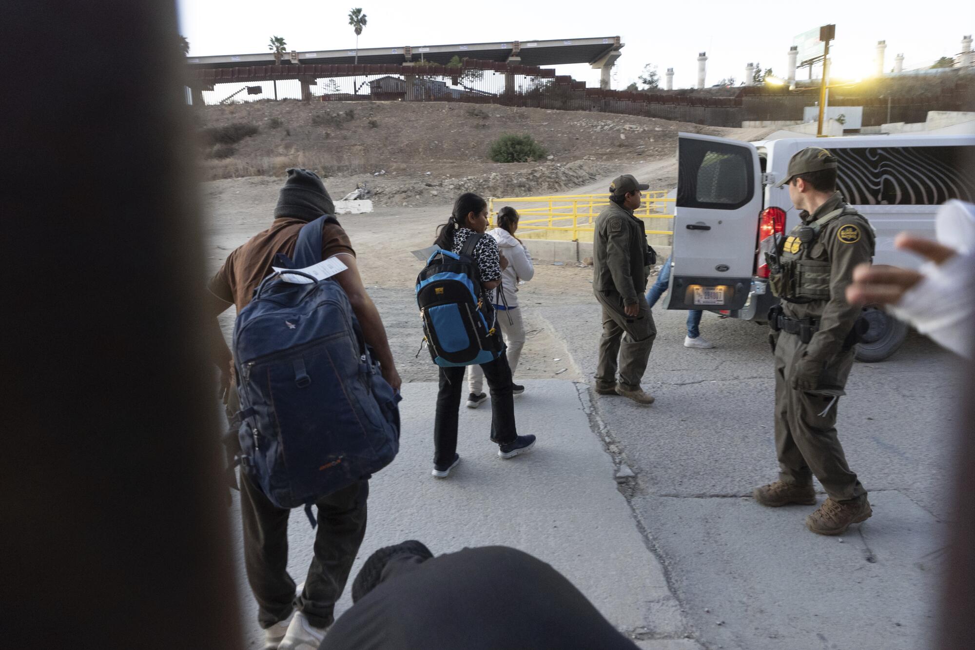 Migrants make their way to a Border Patrol van after crossing illegally into San Diego