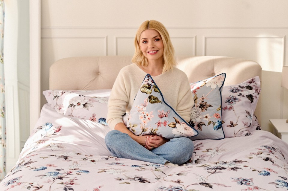 Holly Willoughby sitting on a bed with floral bedding and pillows.