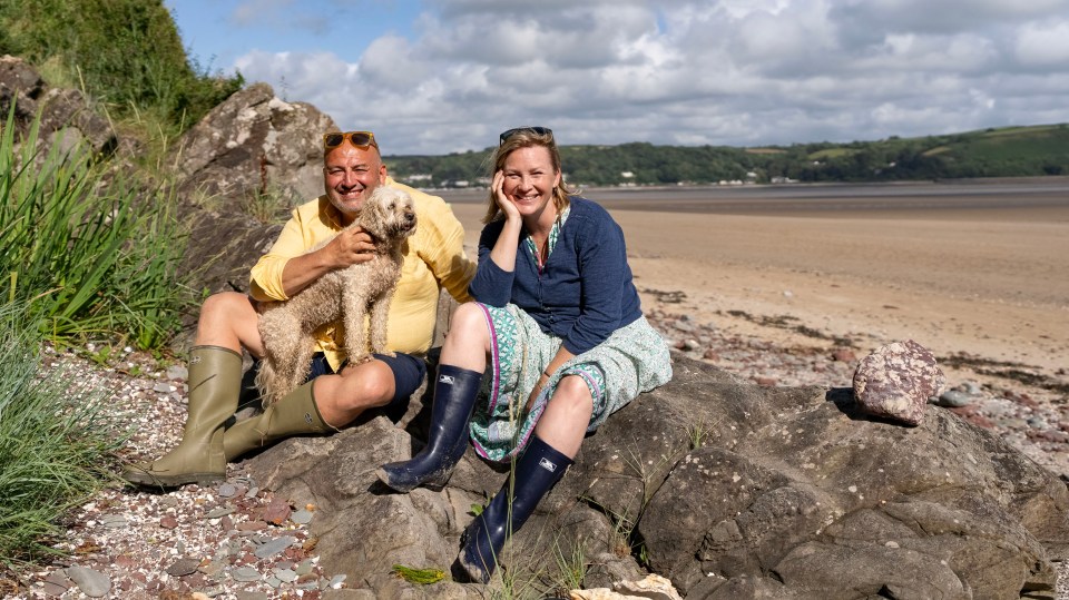 Couple sitting on rocks by the sea with a dog.