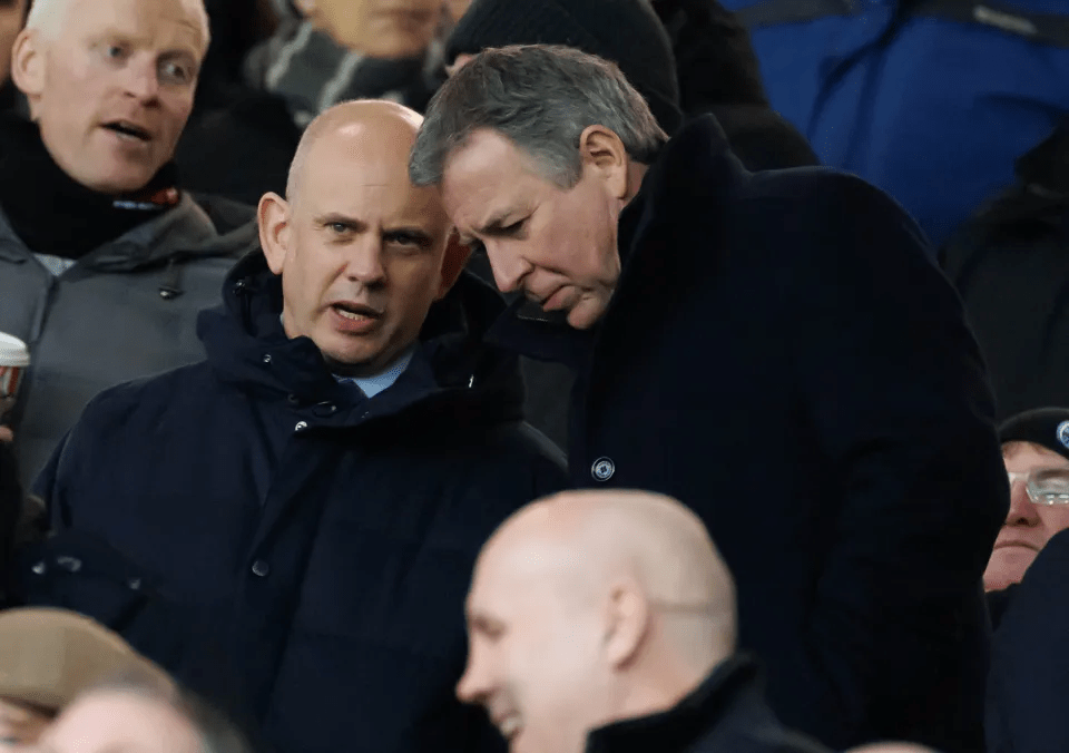 Two men in dark coats talking in a crowd.