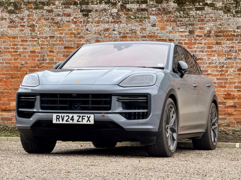 Gray Porsche Cayenne parked in front of a brick wall.