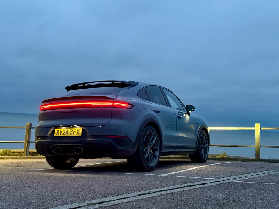 Rear view of a gray Porsche Cayenne parked near the ocean at dusk.