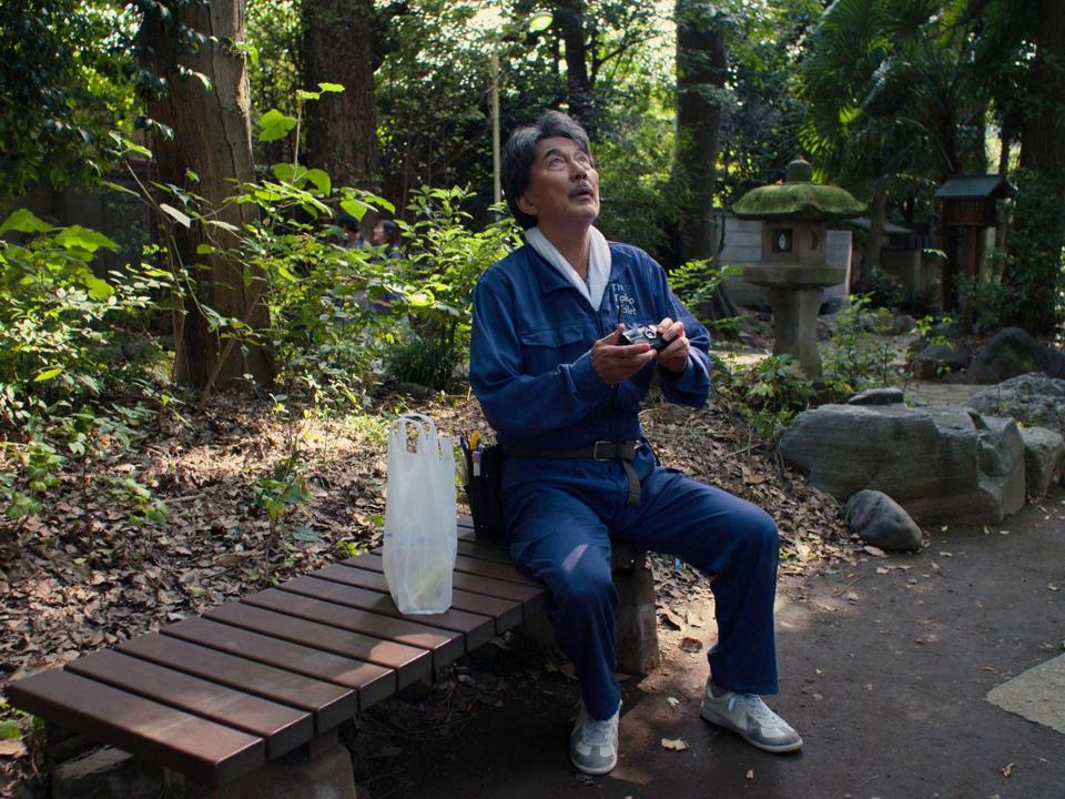 Man sitting on a bench in a park, looking up and holding a camera.