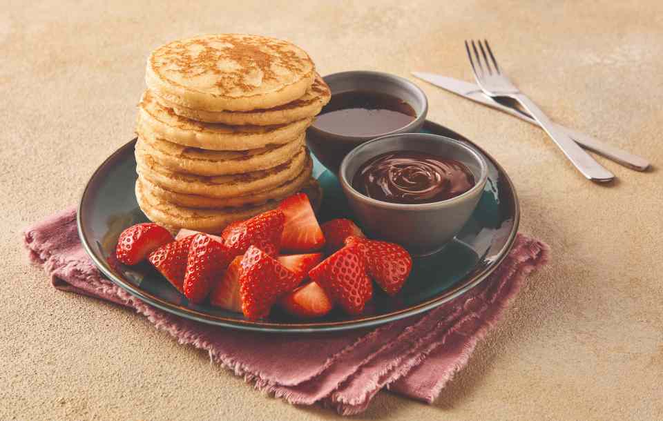 A plate of pancakes, strawberries, and chocolate and maple syrup.