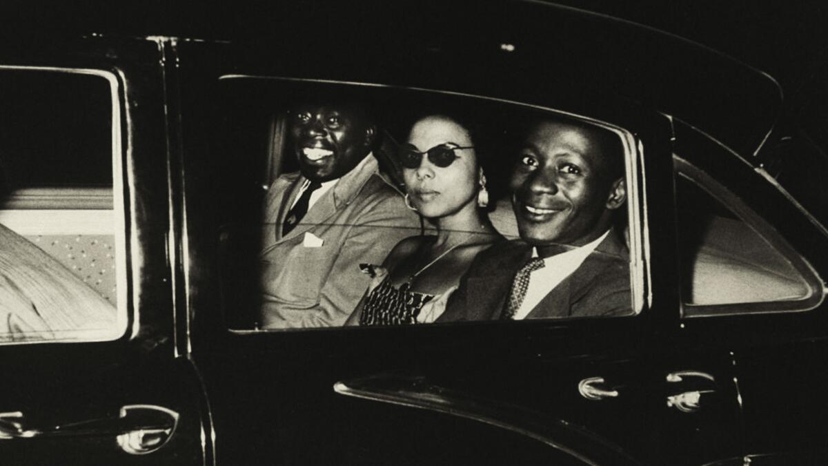 Two men and a woman ride in the back seat of a car.