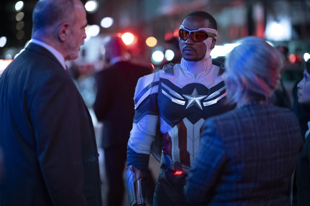 A superhero speaks to two people in suits.