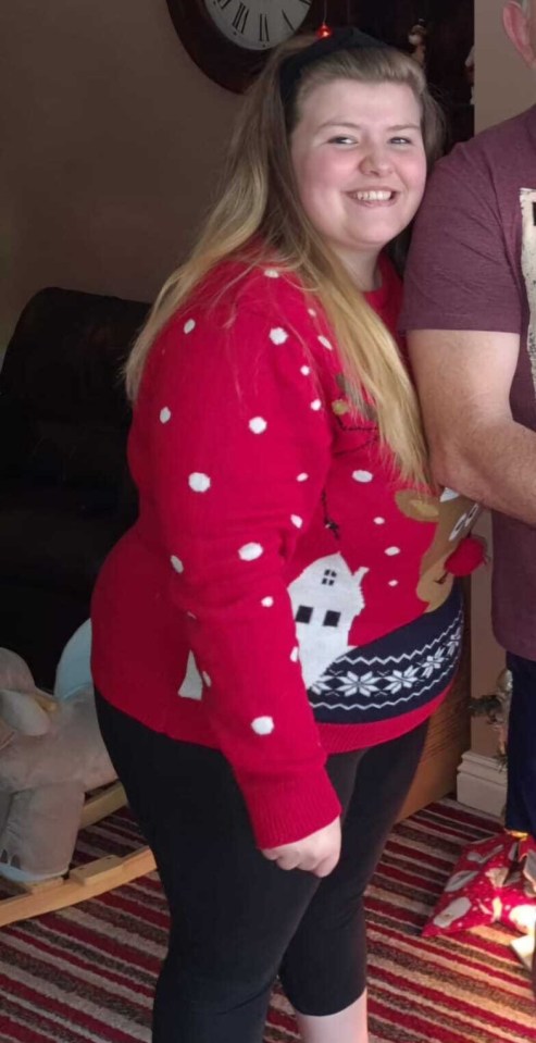 A young woman in a red Christmas sweater and black leggings.