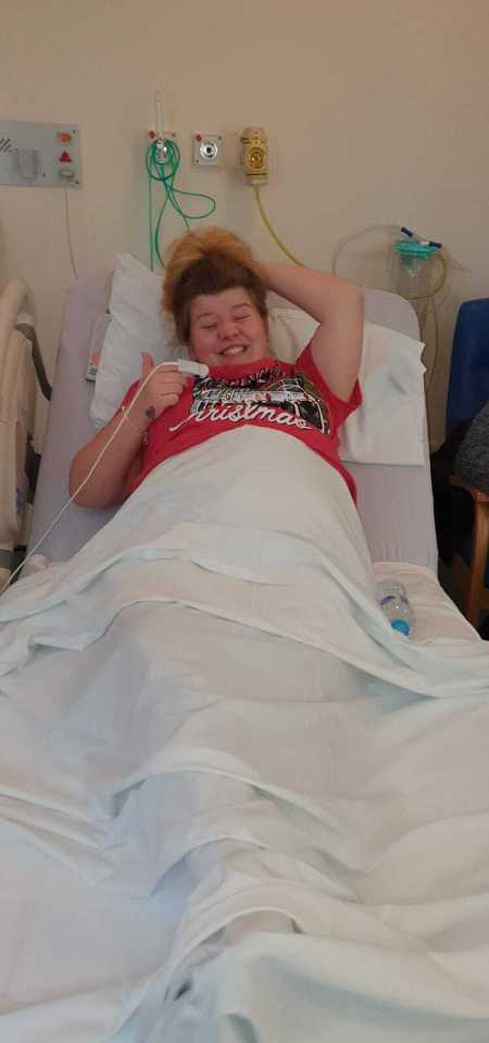 Smiling young woman in a hospital bed giving a thumbs up.