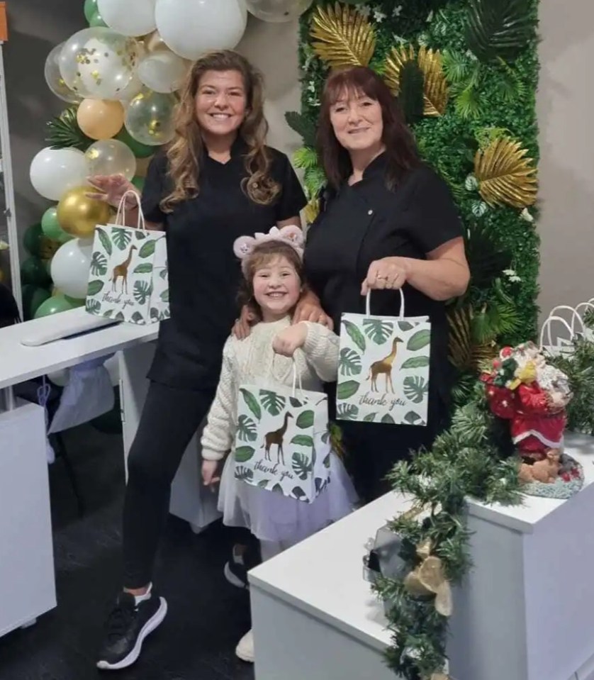 Two women and a young girl stand in a beauty salon, holding gift bags.